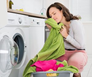 Young Woman Crouching With Cleaned Clothes Near The Electronic Washer